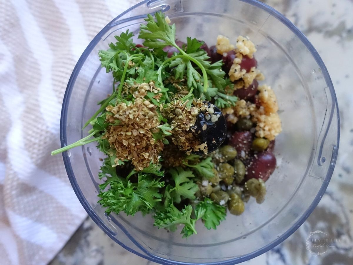 ingredients for olive tapenade in a food processor with parsley oregano kalamata olives and capers