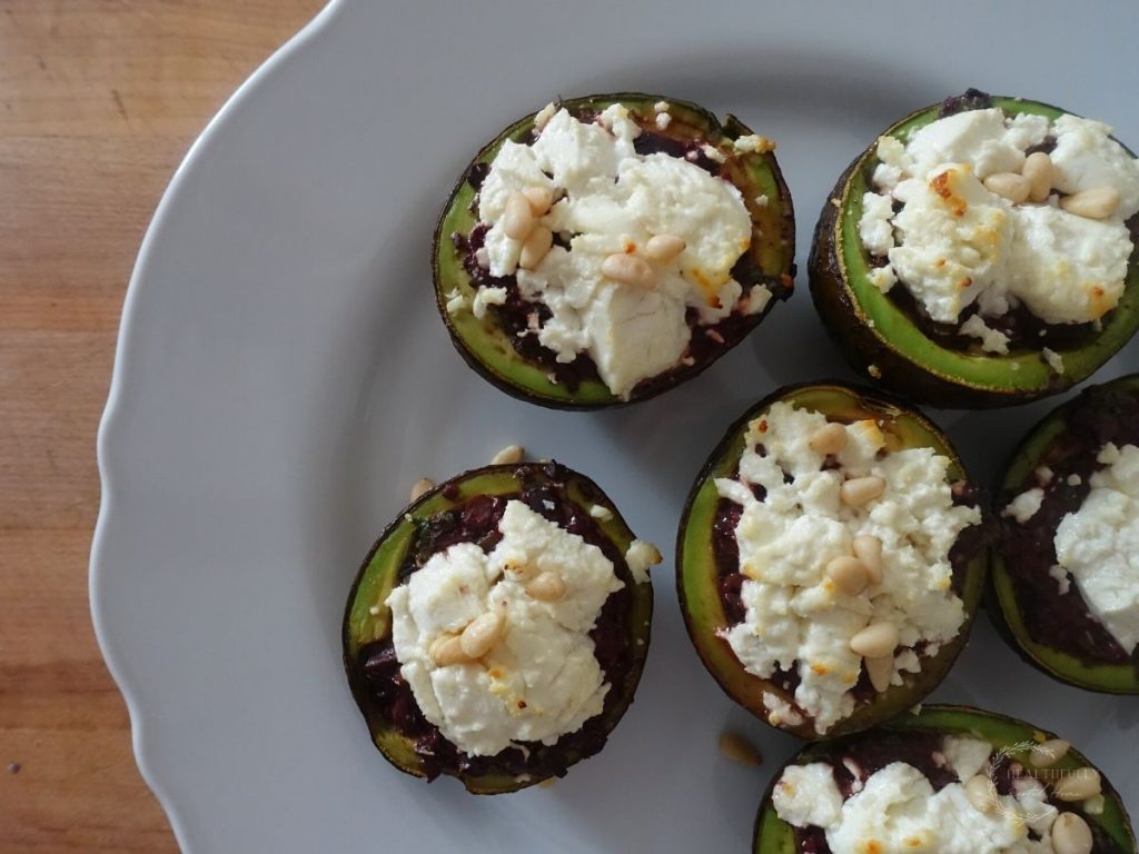 stuffed roasted avocados on a white plate with goat cheese and pine nuts on top