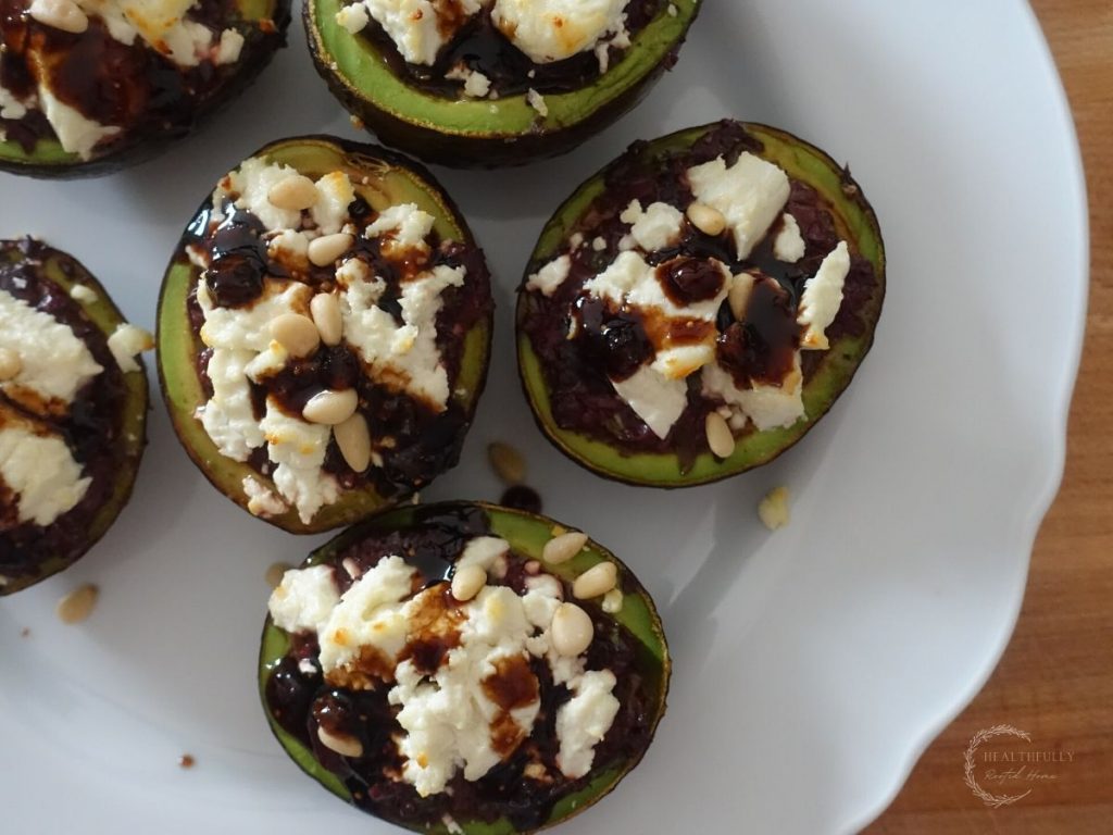 stuffed roasted avocados halved on a white plate with a balsamic fig glaze drizzled on top the goat cheese