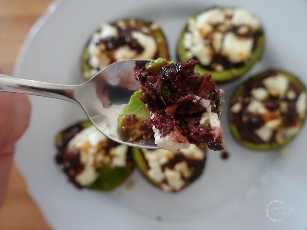 stuffed roasted avocado bite on a spoon with roasted avocados on a white plate in the background