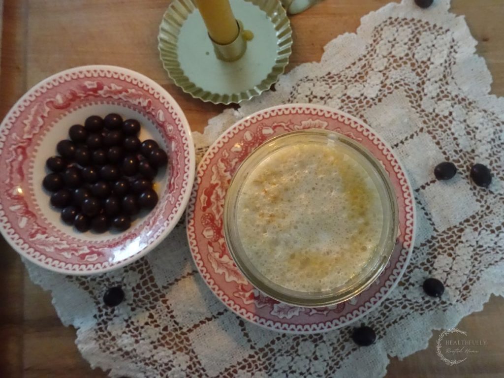 salted caramel cold foam cold brew in a cup with a bowl of chocolate covered espresso beans beside it and a candle and lace doily