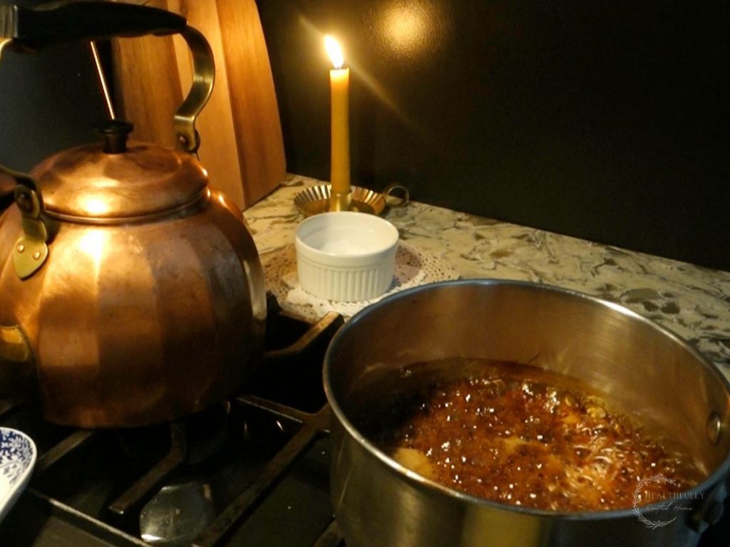 sugar and water melted in a sauce pan to make a caramel sauce with a candle in the background to set the scene and a copper tea kettle