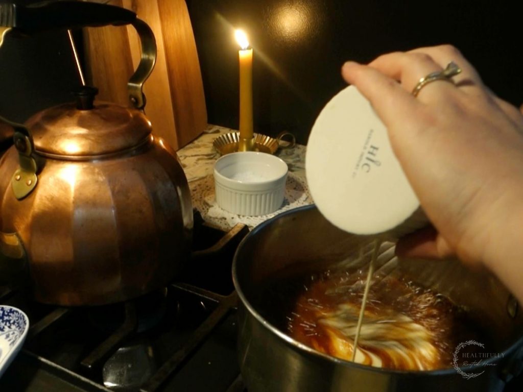 adding cream to the caramel sauce in a sauce pan to make caramel sauce with copper tea kettle behind it