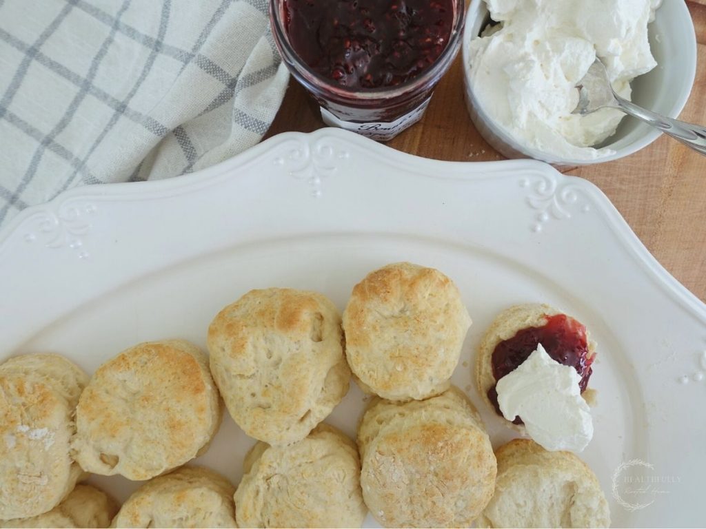 a white platter of lemonade scones with one topped with whipped cream and jam