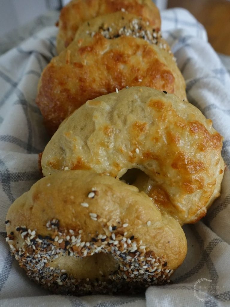 sourdough discard bagels lined up in a basket lined with a ticking striped tea towel some bagels have everything bagel seasoning and some cheddar cheese