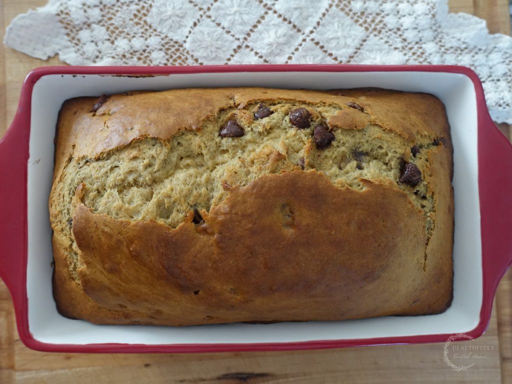 sourdough discard banana bread in a red loaf pan with a lace doily next to it