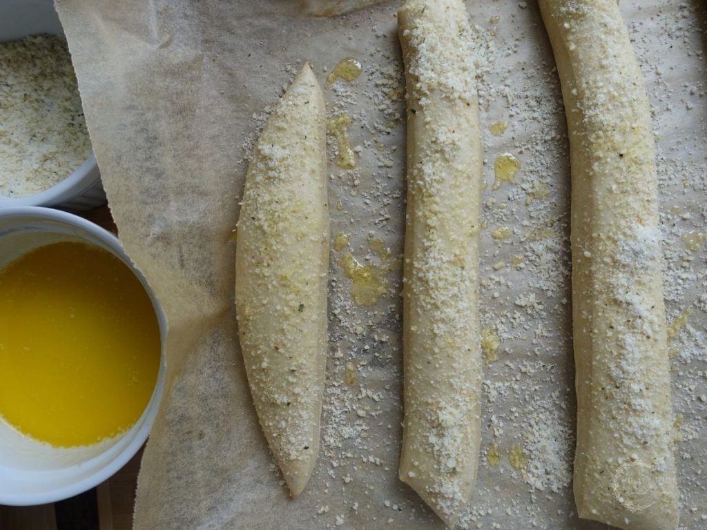 sourdough breadsticks on a parchment lined baking sheet topped with melted butter and garlic parmesan topping
