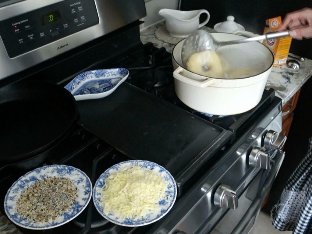 placing a sourdough discard bagel into the pot of boiling water with toppings prepped on the side