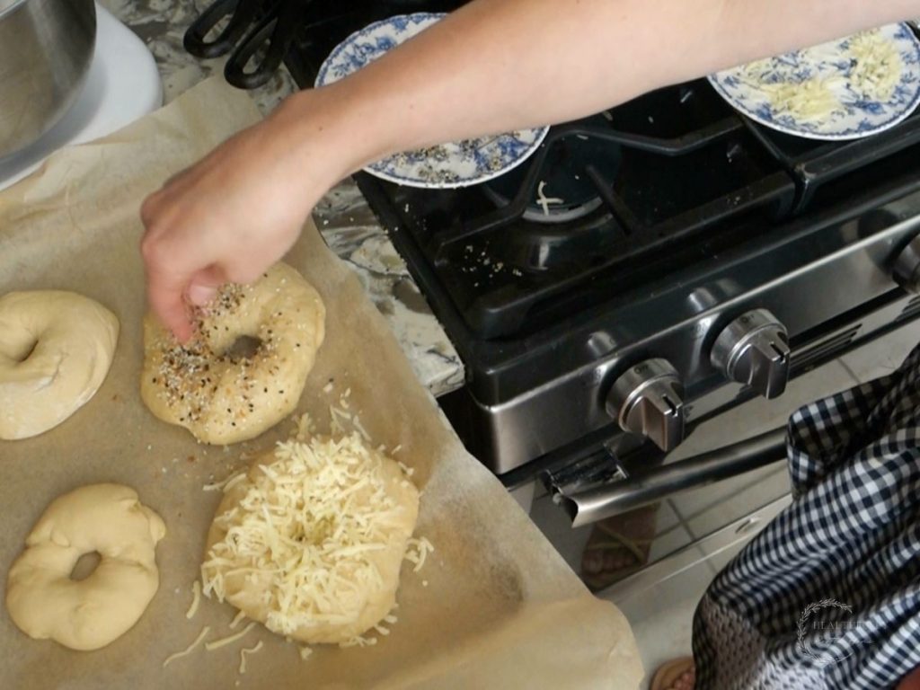 sprinkling toppings on sourdough discard bagels after theyve been pulled out of the boiling water