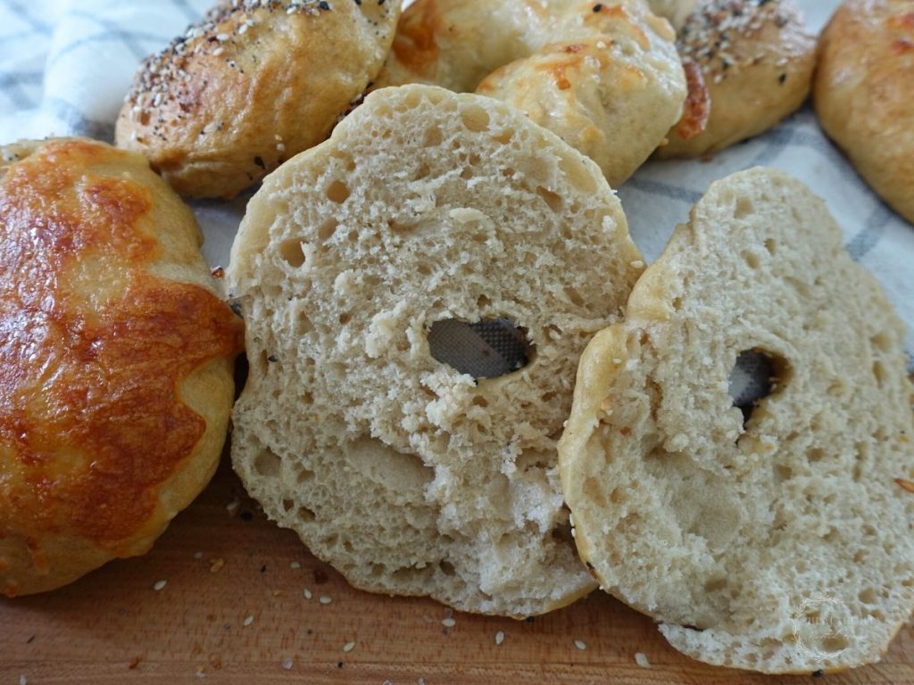 a sourdough discard bagel cut in half so you can see the inside with a bunch of whole bagels surrounding it