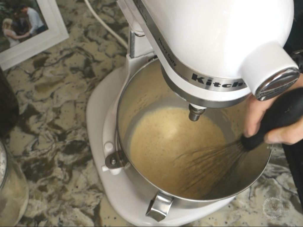 whisking ingredients for sourdough bagel dough in the bowl of a white stand mixer