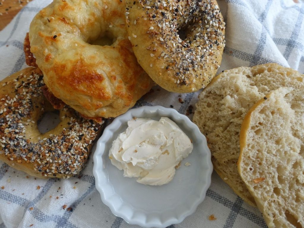 sourdough discard bagels lined up on a towel with a jar of cream cheese and one sliced open
