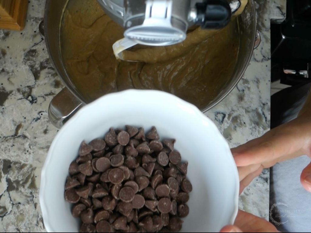 adding chocolate chips to the sourdough discard banana bread batter in a stand mixer
