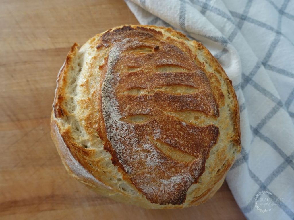 sourdough discard bread loaf on a wooden cutting board next to a tea towel