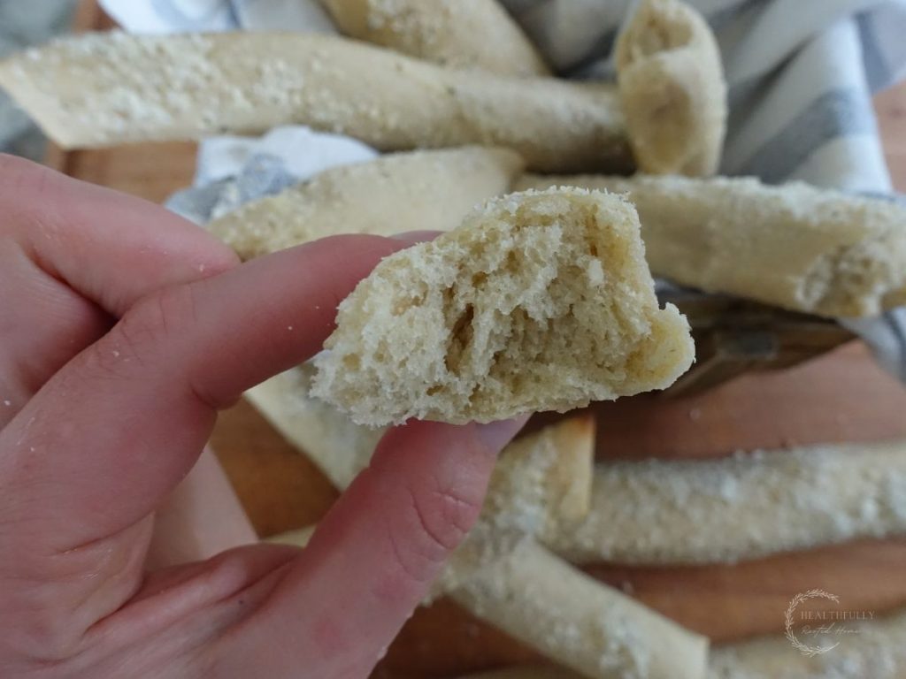 fingers holding up a sourdough breadstick that has a bite taken out of it so you can see how soft it is inside