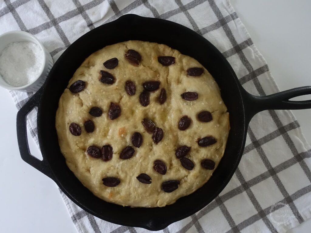 baked sourdough discard focaccia bread in a cast iron skillet with a bowl of sea salt on the side