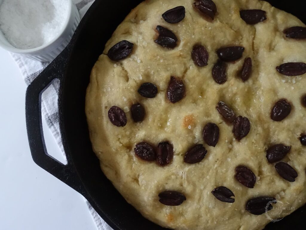 close up of sourdough discard focaccia in a cast iron skillet with kalamata olives dotted on top