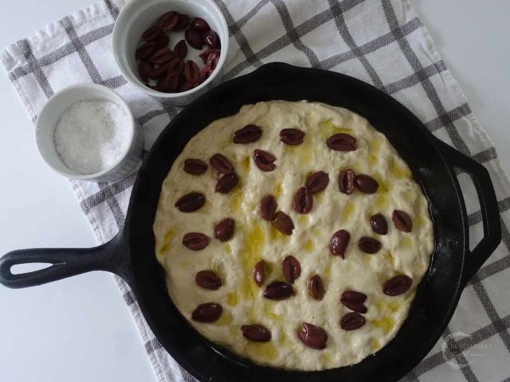 same day sourdough discard focaccia bread unbaked simpled with olive oil and kalamata olives in a cast iron skillet