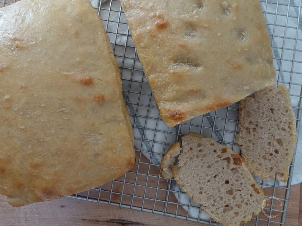 long fermented sandwich bread cooling on a wire cooling rack with a couple slices lying next to two larger loaves