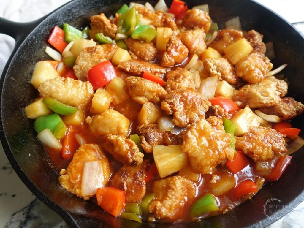 sweet and sour chicken in a cast iron skillet with bell peppers onions and pineapple