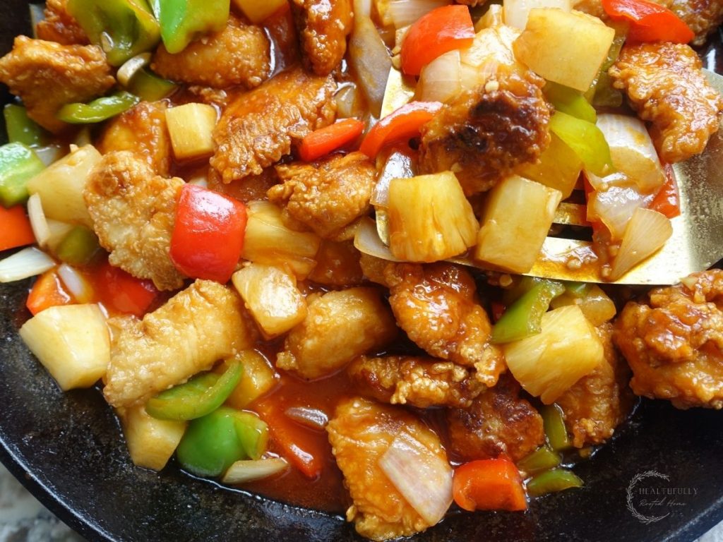 sweet and sour chicken hong kong style in a cast iron skillet with a gold spatula scooping some up to show the detail