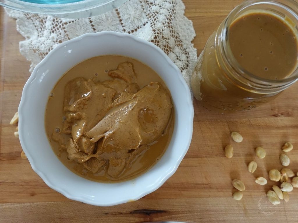 peanut butter in a white bowl sweetened condensed milk in a mason jar and peanuts on the side with a doily in the background