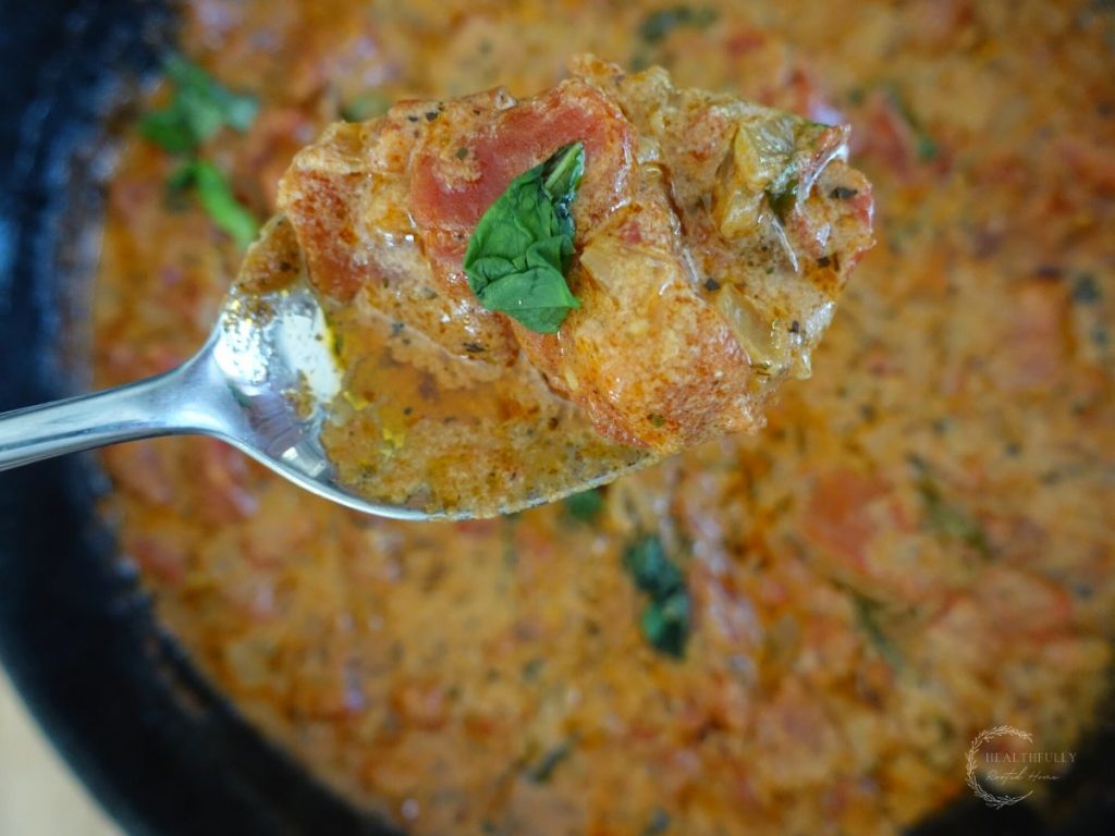 tomato mascarpone sauce in a cast iron skillet with a spoonful of sauce close up and a piece of basil on top