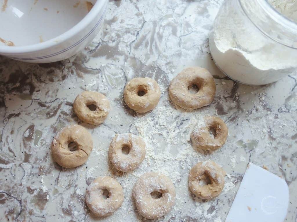 sourdough donut dough shaped into donuts with a glass jar of flour and a dough scraper nearby