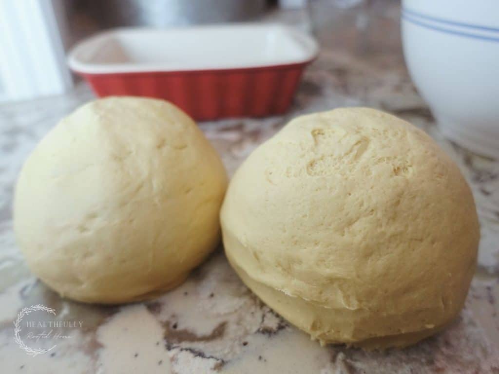 two balls of einkorn sourdough with a red loaf pan in the back