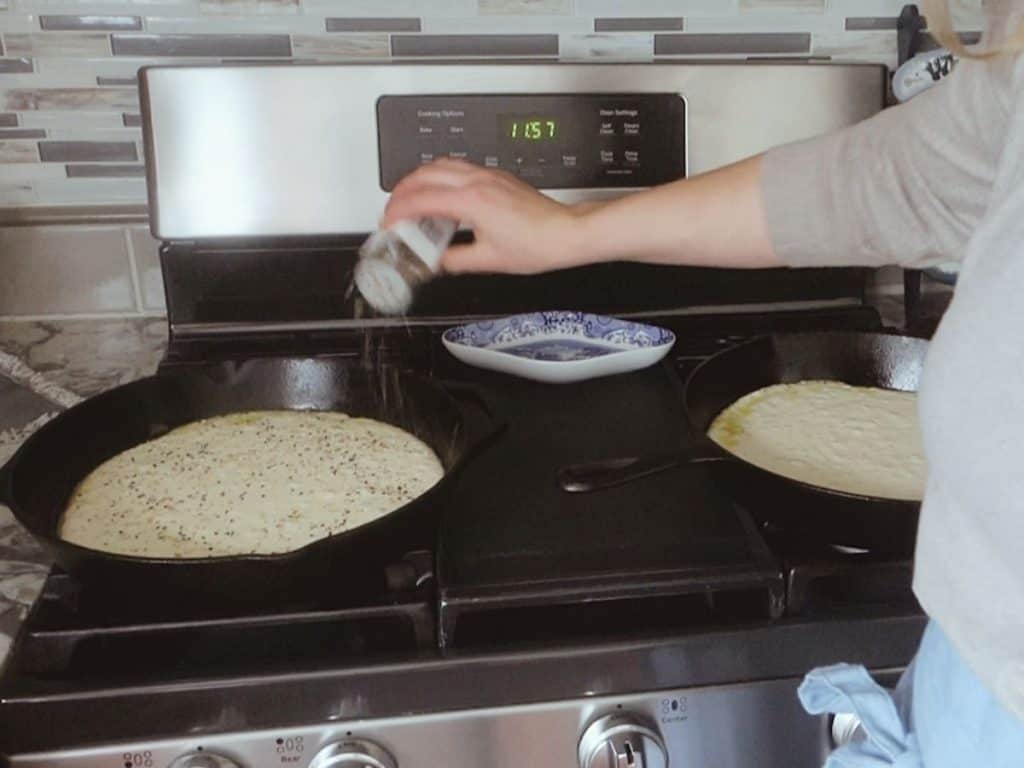 sprinkling everything bagel seasoning over top sourdough starter while it's in a cast iron skillet