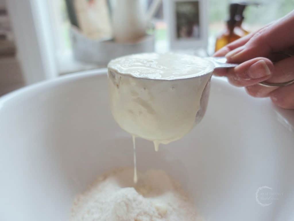 sourdough starter filled measuring cup with starter dripping from the bottom into a ceramic bowl with einkorn flour