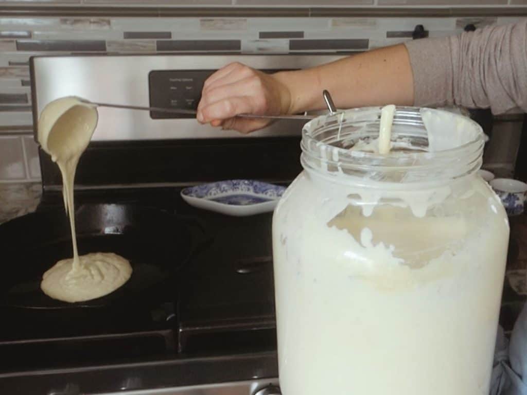 sourdough starter being poured into a hot cast iron skillet using a ladle