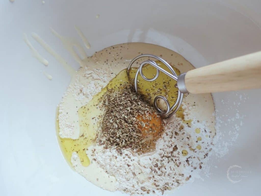 sourdough starter dried herbs einkorn flour egg and baking soda in a ceramic bowl with a danish dough whisk