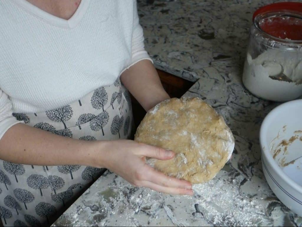 flattening out sourdough donut dough on a floured surface wearing a white sweater and apron