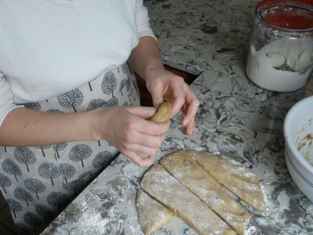 using thumb and forefinger to shape sourdough donuts into donuts with strips of dough on the counter