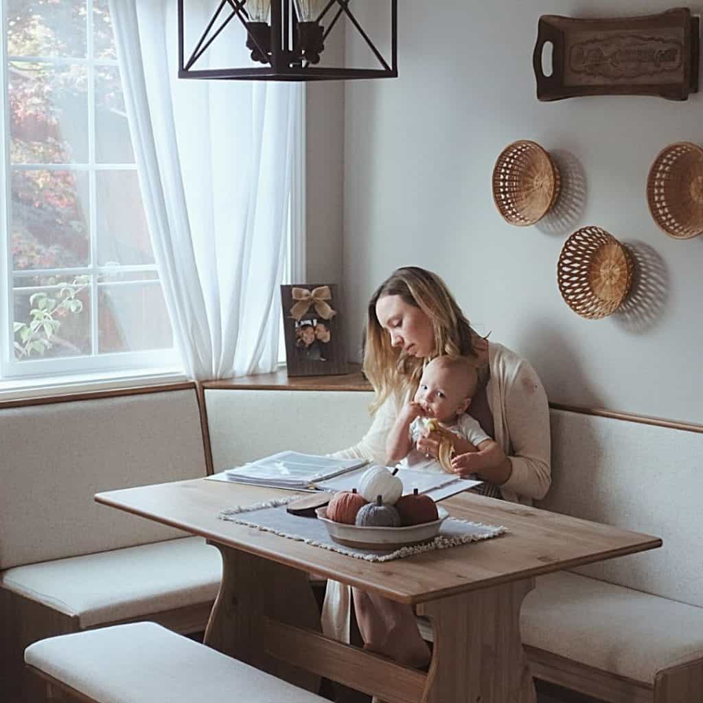 autumn homemaker sitting in a breakfast nook with baby looking at meal plan book