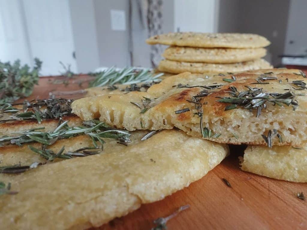 sourdough discard flatbread on a boos block cutting board stacked on top of eachother with herbs