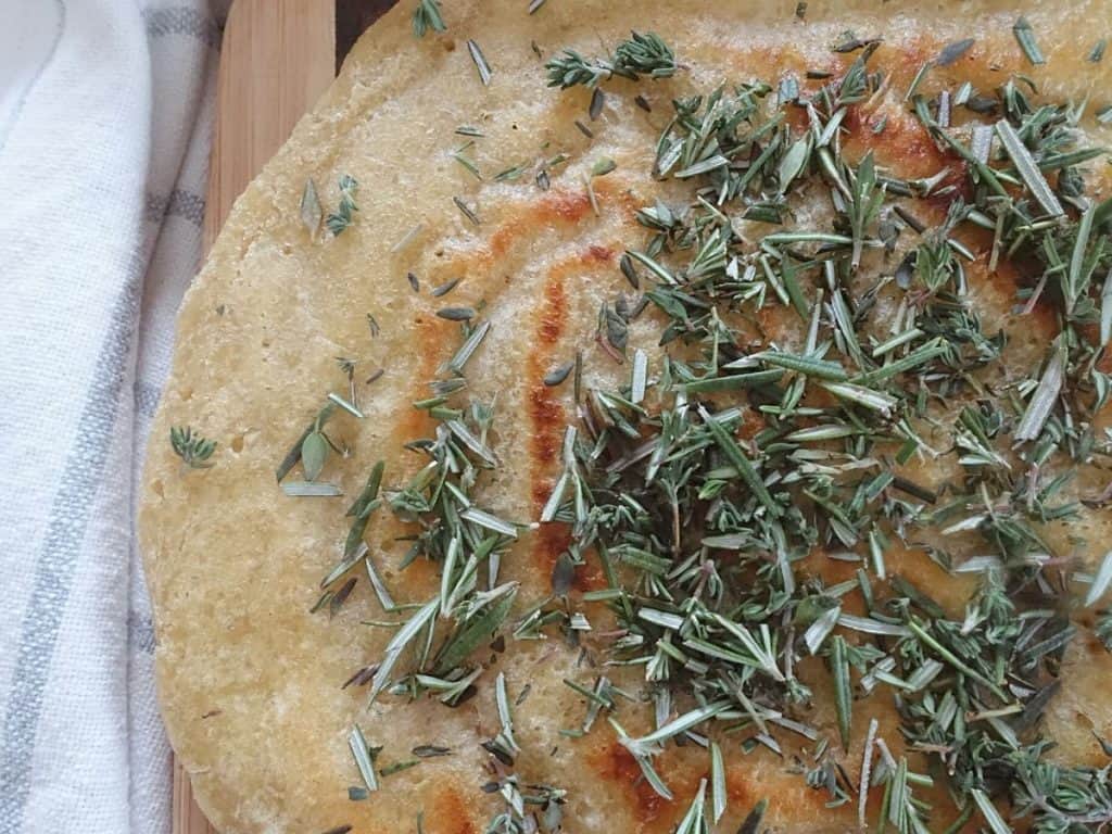 sourdough discard flatbread with dried herbs on top next to a blue and white striped tea towel