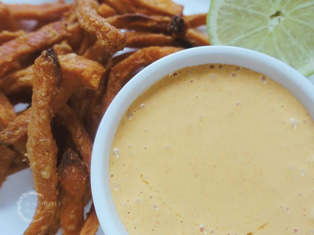 ancho aioli in a white dish next to a halved lime and sweet potato fries