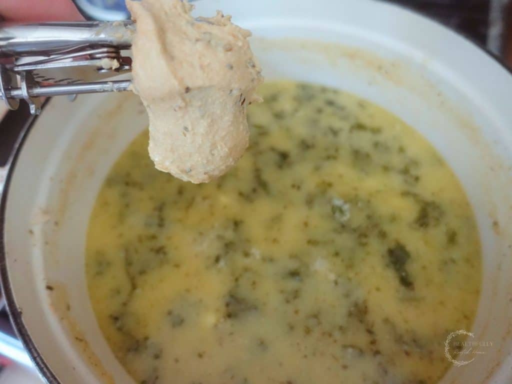 dropping sourdough dumpling batter into a pot of kale and chicken soup in a white dutch oven