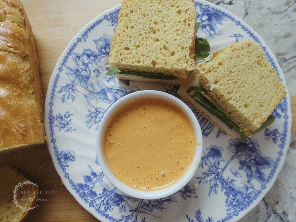 ancho aioli in a dish next to a sandwich on top of a blue plate with a load of sourdough sandwich bread next to it