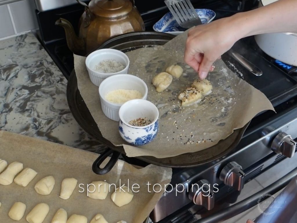 sprinkling everything bagel seasoning, parmesan cheese and sea salt onto the boiled sourdough pretzel bites