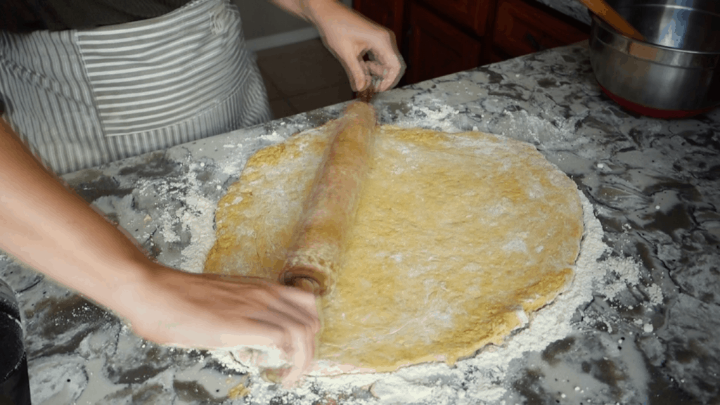 rolling out pumpkin sourdough cinnamon roll dough on a lightly floured surface with wooden rolling pin