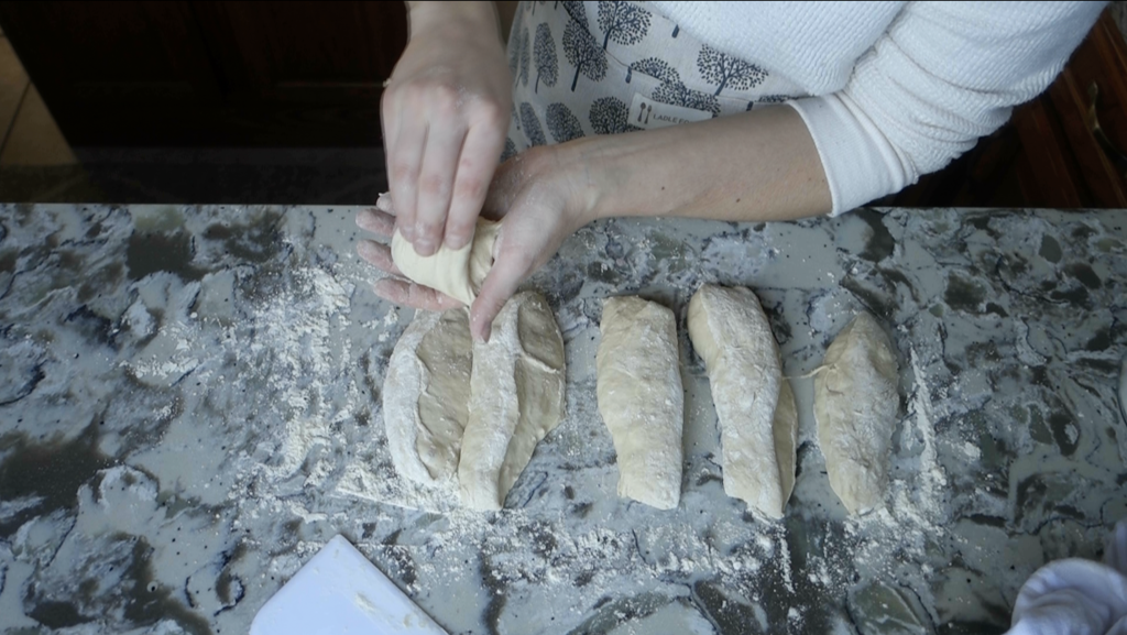 ball of sourdough being shaped into a bun with strips of dough beneath it