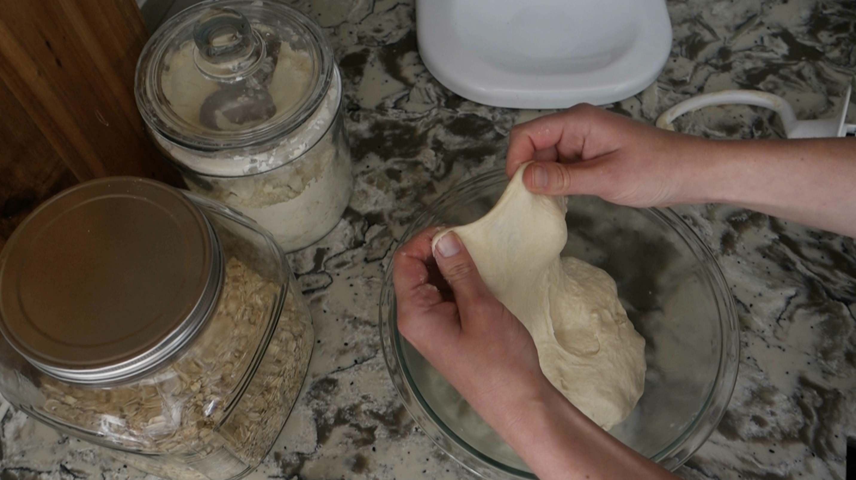 doing the windowpane test with sourdough pretzel dough inside of a glass bowl next to a white stand mixer