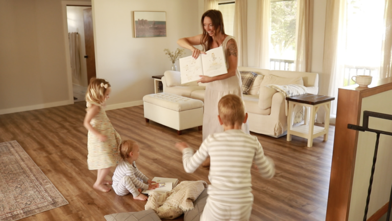 A Christian homemaker in a light gingham dress reads to her small children on the floor of their living room.