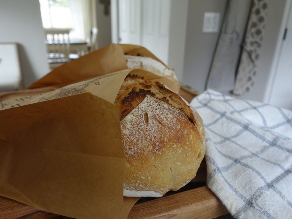 fresh loaves of homemade sourdough bread in brown paper bags with a blue and white tea towel next to them