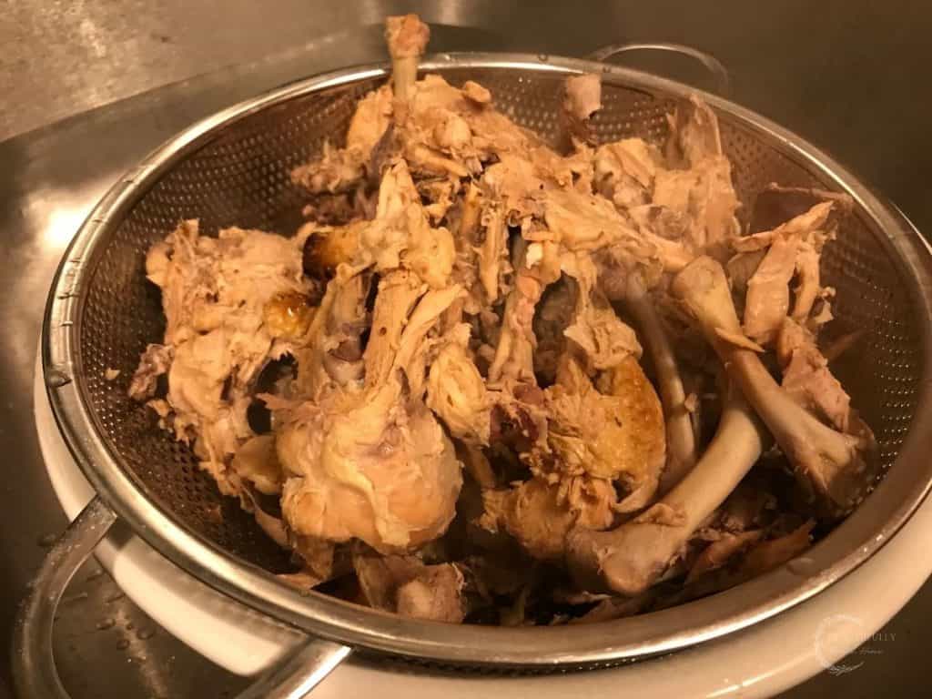 chicken bones in a stainless steel strainer to remove the bone broth