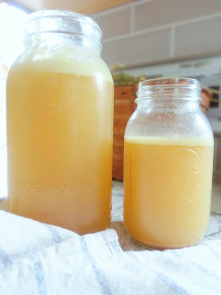 homemade bone broth in mason jars with fat separated and a blue and white striped tea towel in front