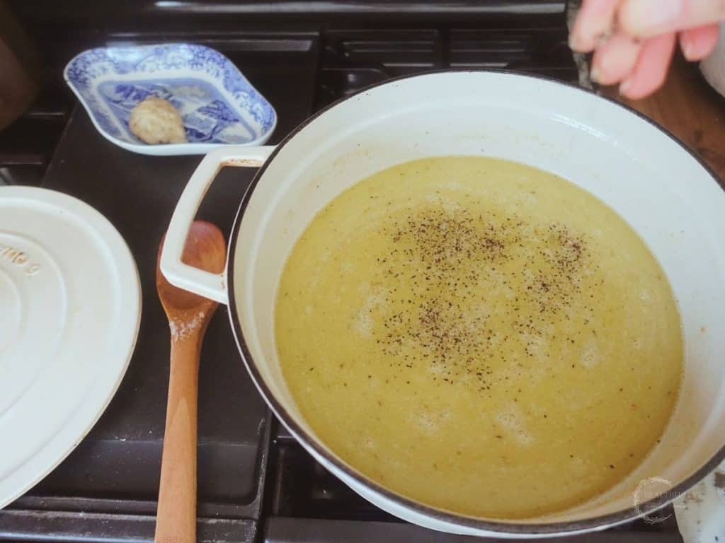 adding spices to chicken collagen soup in a white dutch oven with wooden spoon next to it
